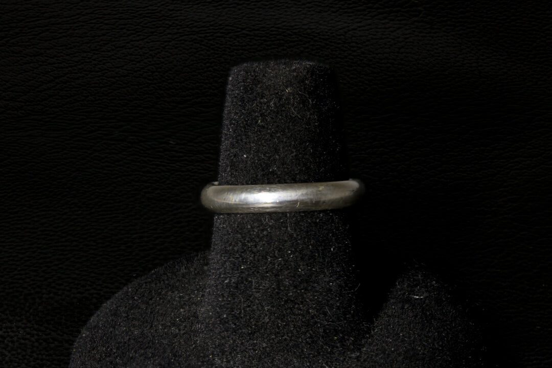 Silver ring on a black textured stand against a dark background back view