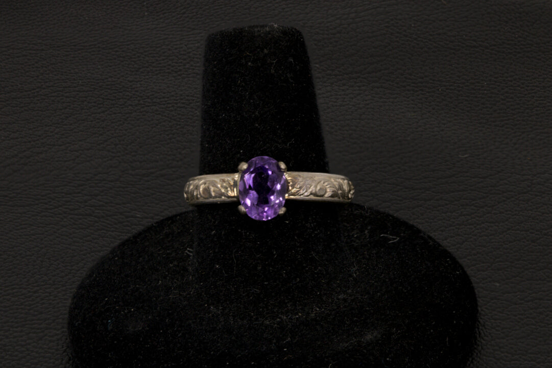 Amethyst oval ring with decorative ring band prong set in sterling silver on a black stand