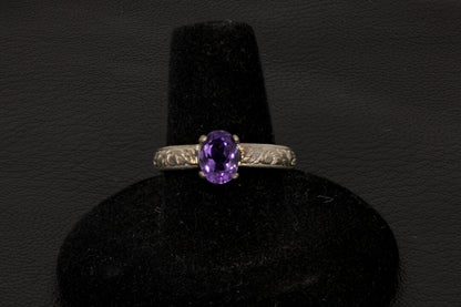 Amethyst oval ring with decorative ring band prong set in sterling silver on a black stand
