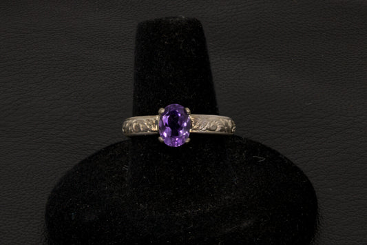 Amethyst oval ring with decorative ring band prong set in sterling silver on a black stand