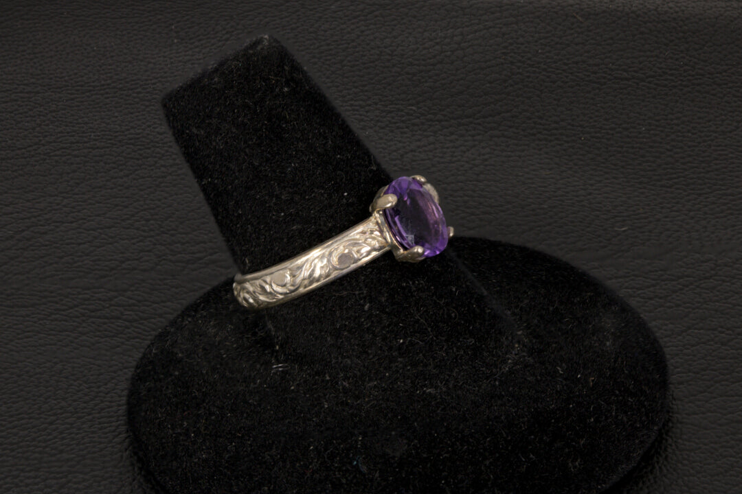 Amethyst oval ring with decorative ring band prong set in sterling silver on a black stand