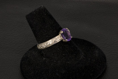Amethyst oval ring with decorative ring band prong set in sterling silver on a black stand