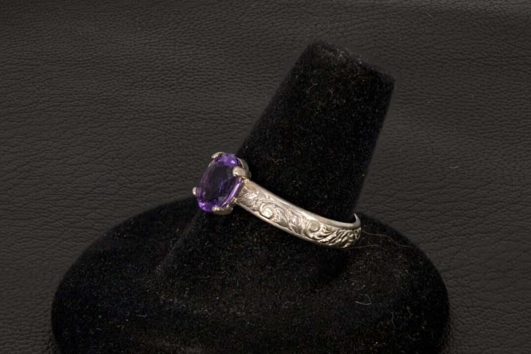Amethyst oval ring with decorative ring band prong set in sterling silver on a black stand