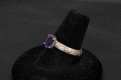 Amethyst oval ring with decorative ring band prong set in sterling silver on a black stand