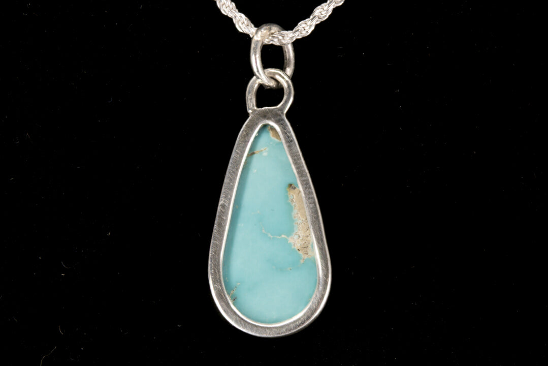 Teardrop-shaped turquoise pendant on a silver chain against a black background back view