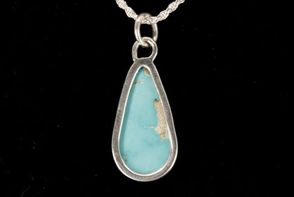 Teardrop-shaped turquoise pendant on a silver chain against a black background back view