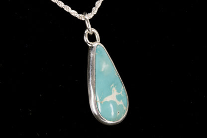Teardrop-shaped turquoise pendant on a silver chain against a black background right side view