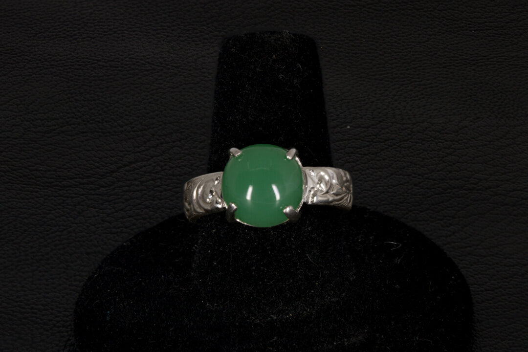 Silver ring with a green gemstone on a black stand against a dark background