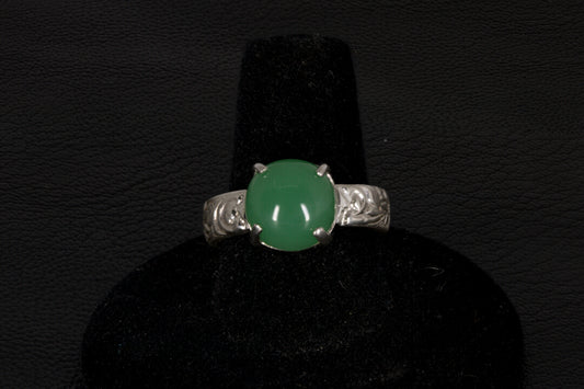 Silver ring with a green gemstone on a black stand against a dark background