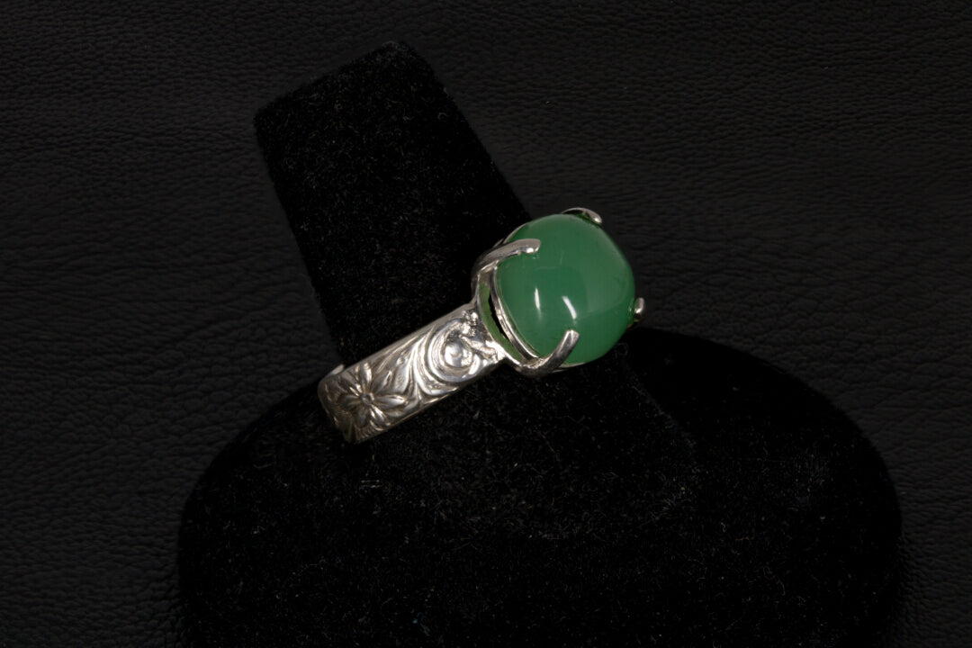 Silver ring with a green gemstone on a black stand against a dark background