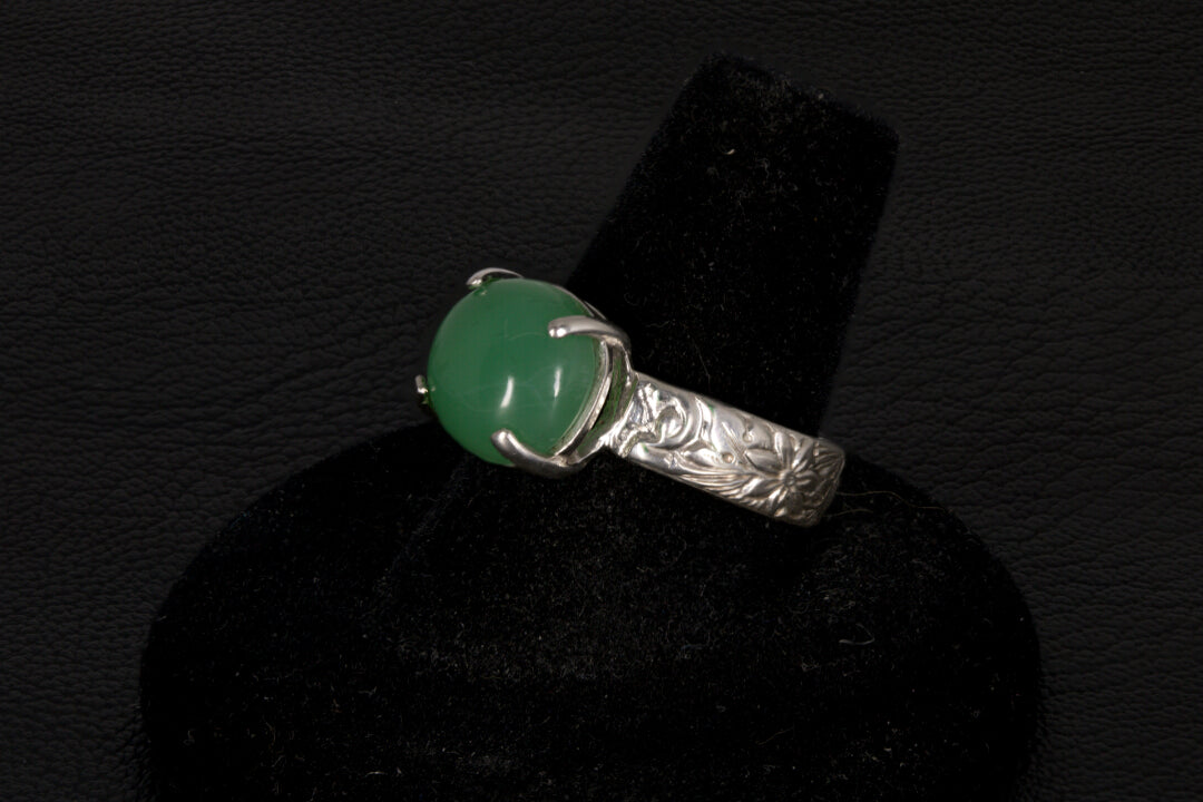 Silver ring with a green gemstone on a black stand against a dark background