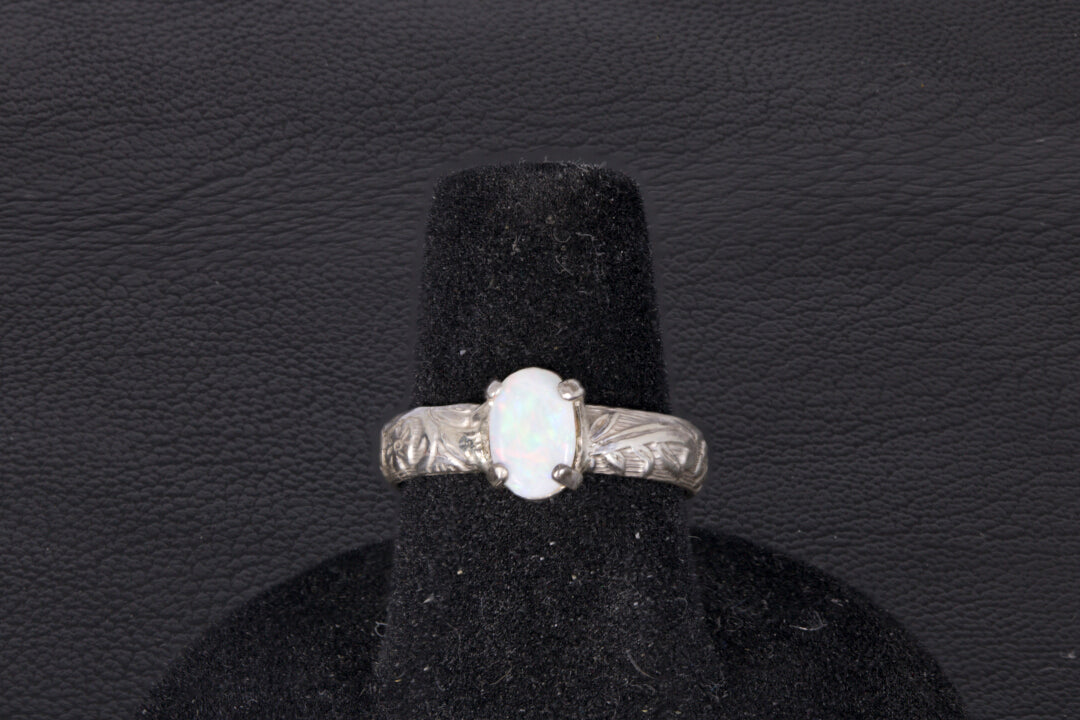 Silver ring with a central oval Opal on a black stand against a dark background