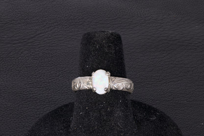 Silver ring with a central oval Opal on a black stand against a dark background