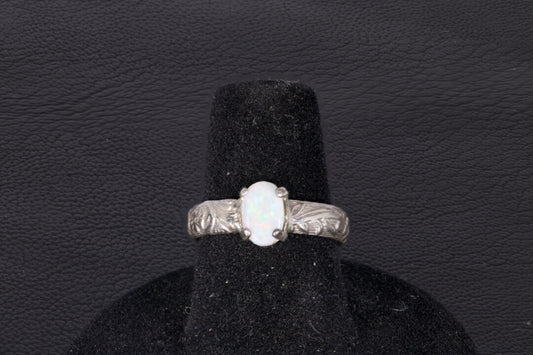 Silver ring with a central oval Opal on a black stand against a dark background