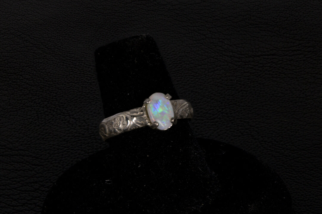 Silver ring with a central oval Opal on a black stand against a dark background