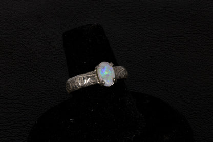 Silver ring with a central oval Opal on a black stand against a dark background