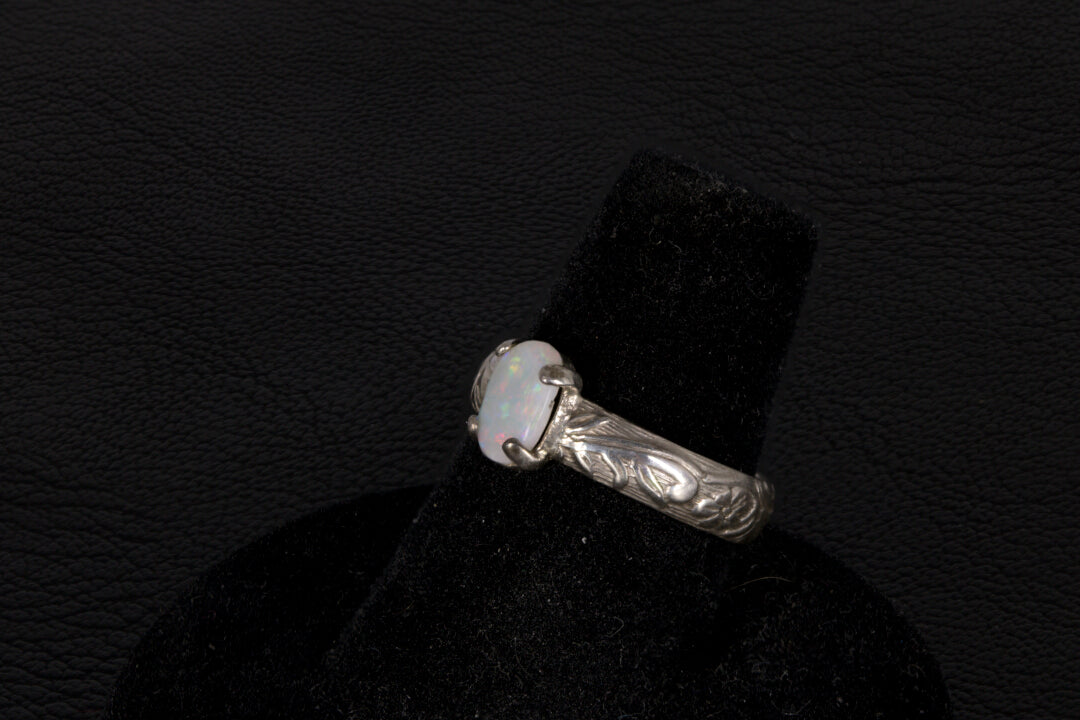 Silver ring with a central oval Opal on a black stand against a dark background