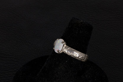 Silver ring with a central oval Opal on a black stand against a dark background