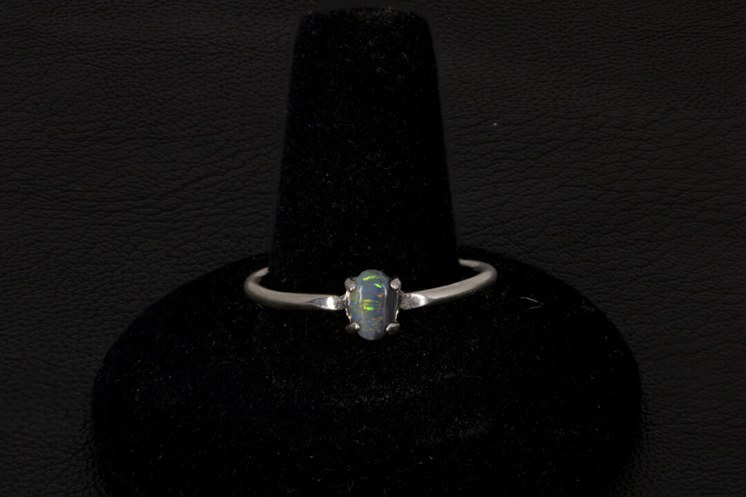 Small dark base opal ring set in sterling silver on a black stand on a black background