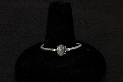 Small dark base opal ring set in sterling silver on a black stand on a black background