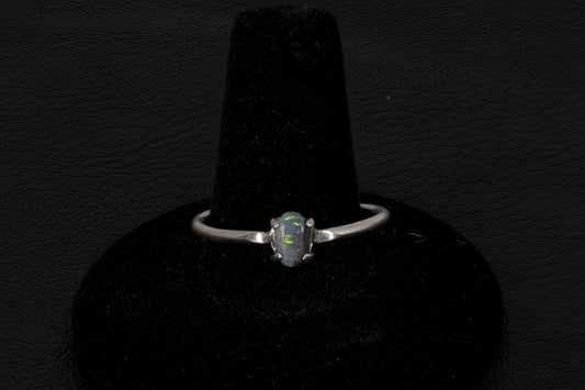 Small dark base opal ring set in sterling silver on a black stand on a black background