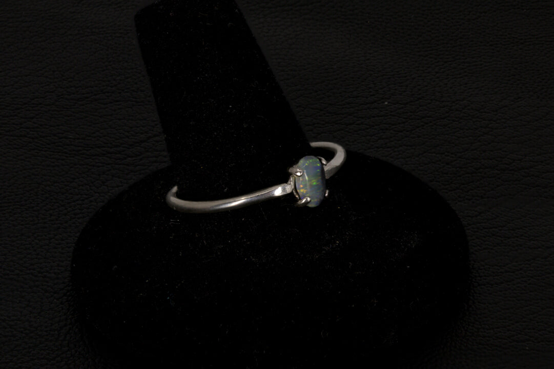 Small dark base opal ring set in sterling silver on a black stand on a black background