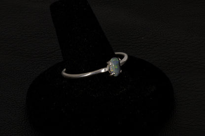 Small dark base opal ring set in sterling silver on a black stand on a black background