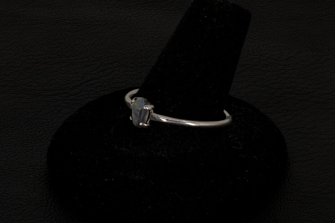 Small dark base opal ring set in sterling silver on a black stand on a black background