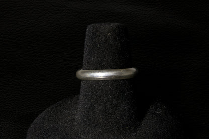 Silver ring on a black textured stand against a dark background back view