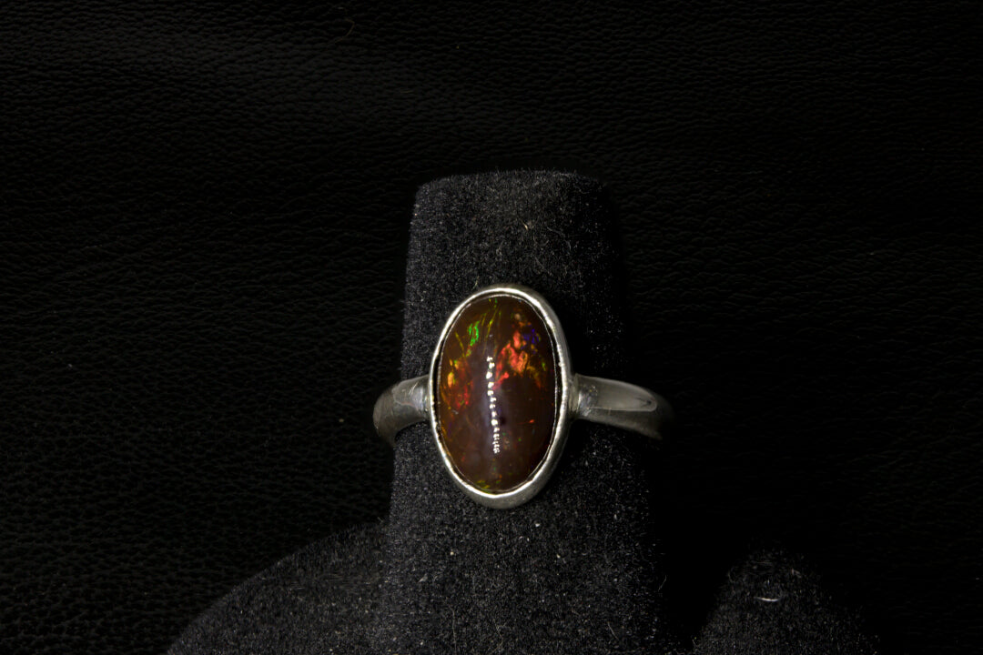 Silver ring with an oval gemstone on a black stand against a dark background