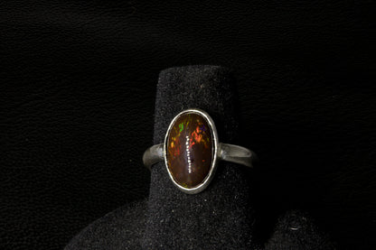 Silver ring with an oval gemstone on a black stand against a dark background