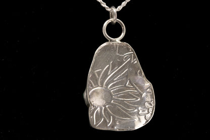 Silver pendant with sun design on a black background, back of pendant