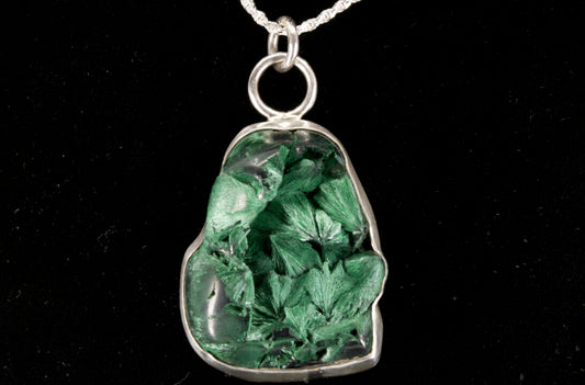 Green mineral stone pendant on a silver chain against a black background front view