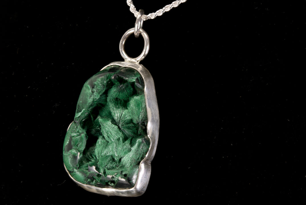 Green stone pendant on a silver chain against a black background left side view