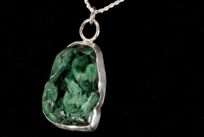 Green stone pendant on a silver chain against a black background left side view