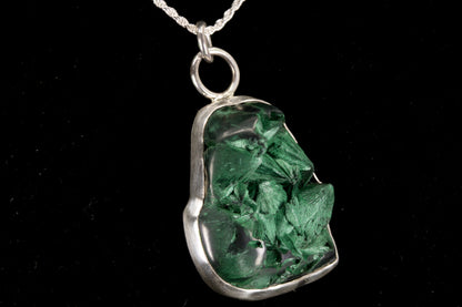 Green crystal pendant on a silver chain against a black background right side view