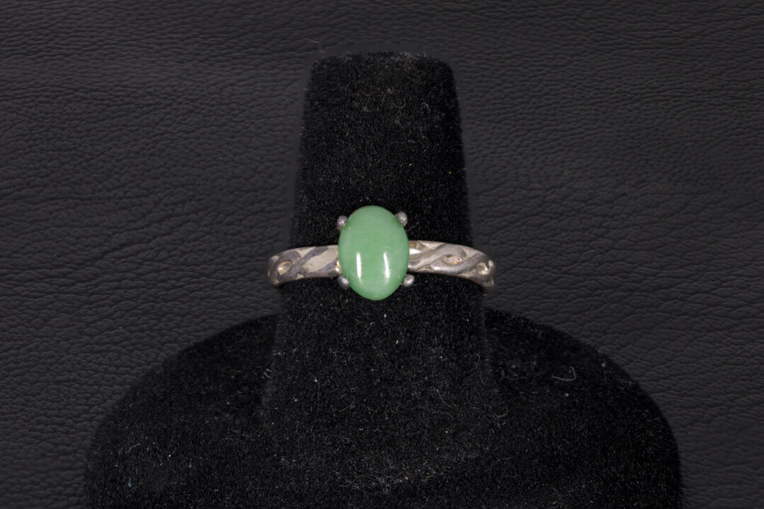 Green Jade ring set in sterling silver with a decorative infinity ring band on a black stand