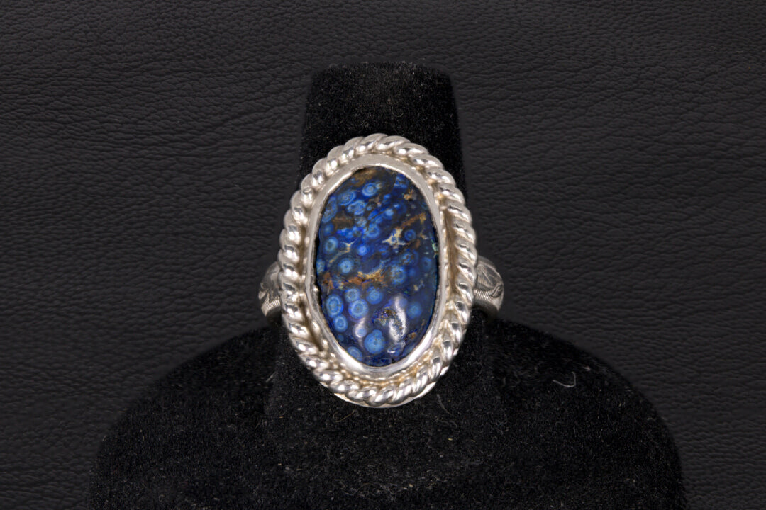 Silver ring with a blue stone on a black stand against a dark background