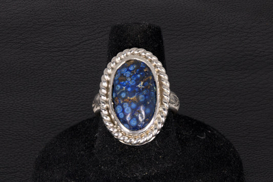 Silver ring with a blue stone on a black stand against a dark background