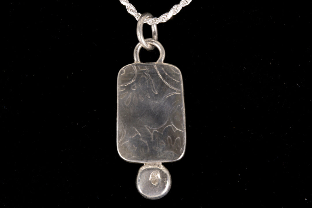 Silver back of pendant on a silver chain against a black background