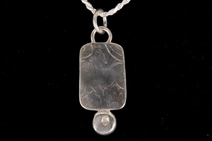 Silver back of pendant on a silver chain against a black background