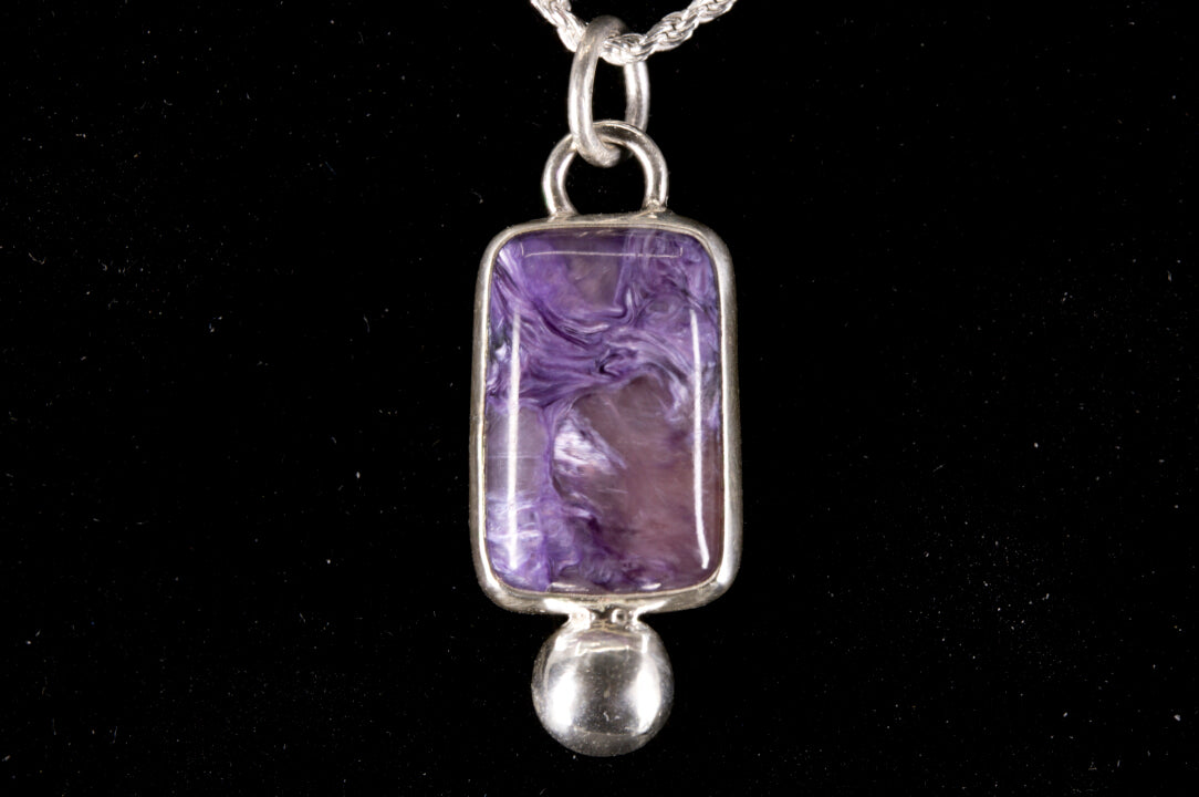 Purple Charoite pendant on a silver chain against a black background front view