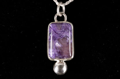 Purple Charoite pendant on a silver chain against a black background front view