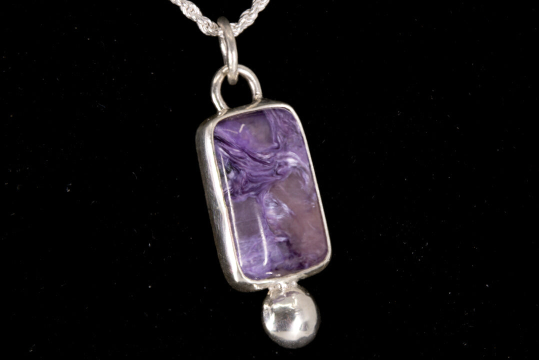 Purple Charoite pendant on a silver chain against a black background left side view