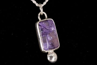 Purple Charoite pendant on a silver chain against a black background left side view