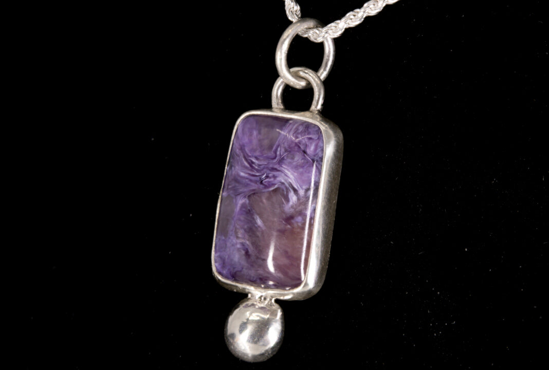 Purple Charoite pendant on a silver chain against a black background right side view