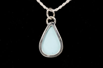 Teardrop-shaped pendant with light blue glass on a silver chain against a black background back view