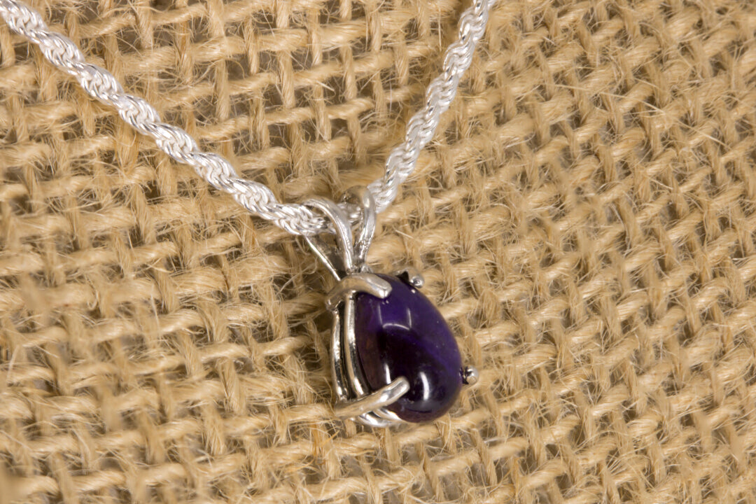 Sugilite pendant necklace on a textured beige background left side view