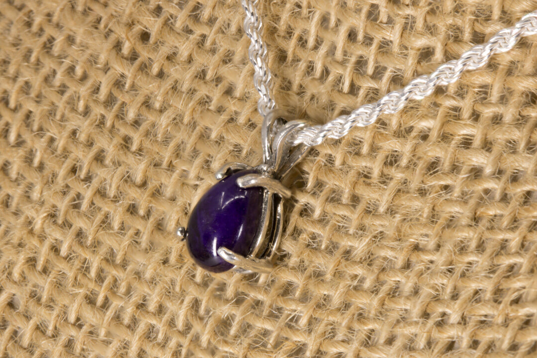 Sugilite pendant necklace on a textured beige background right side view